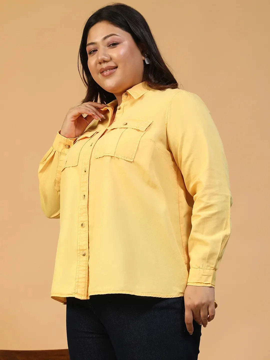 A woman wearing a yellow button-up shirt and black pants is smiling and looking to the side.