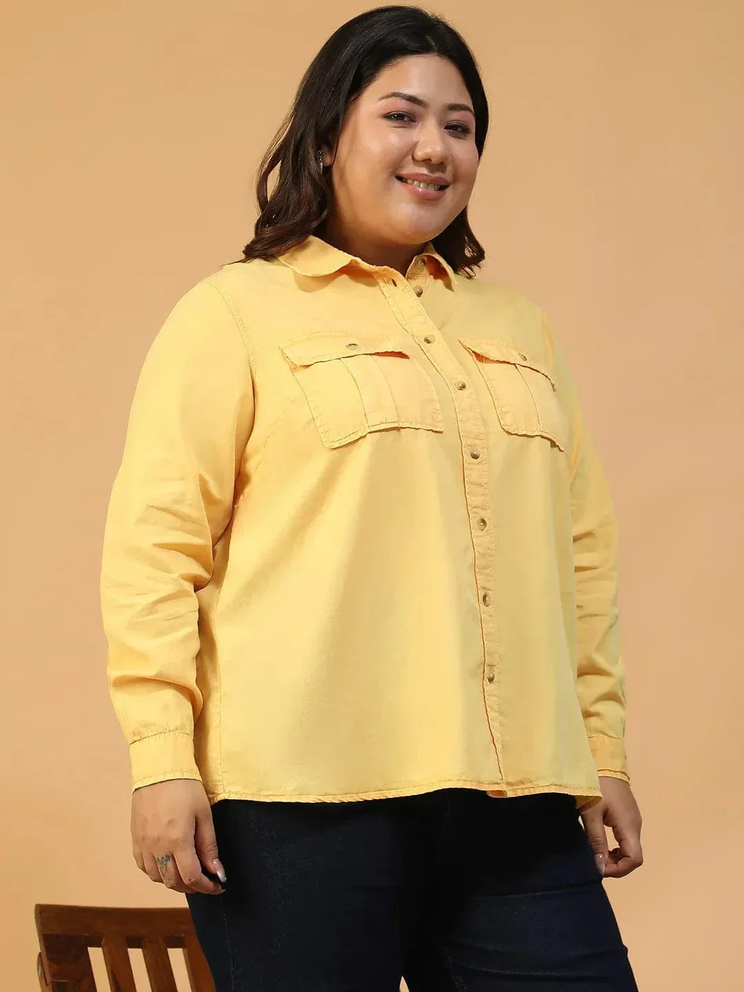A woman wearing a yellow button-up shirt and black pants is smiling and looking to the side.