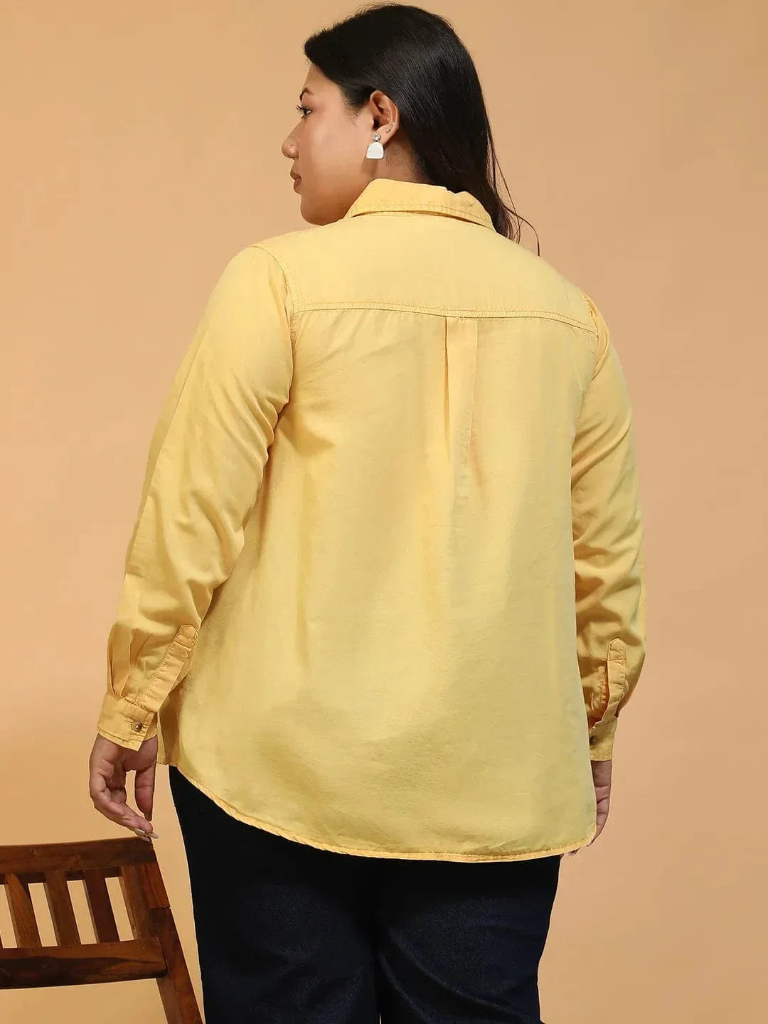A woman wearing a yellow button-up shirt and black pants is smiling and looking to the side.