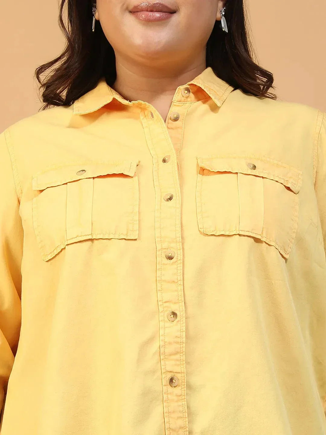 A woman wearing a yellow button-up shirt and black pants is smiling and looking to the side.