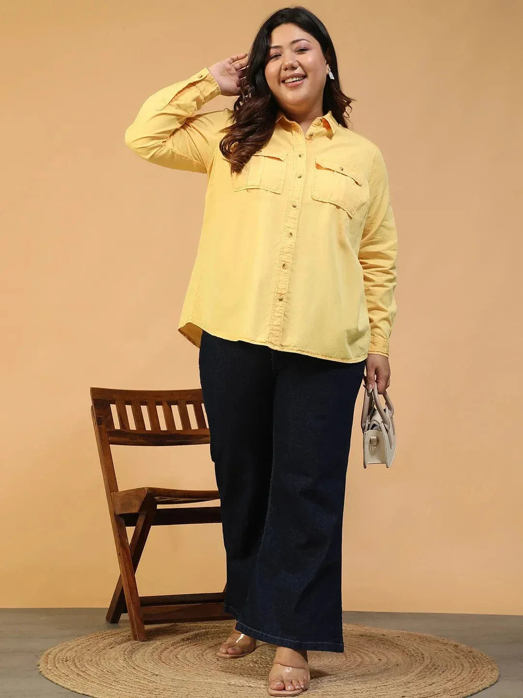 A woman wearing a yellow button-up shirt and black pants is smiling and looking to the side.