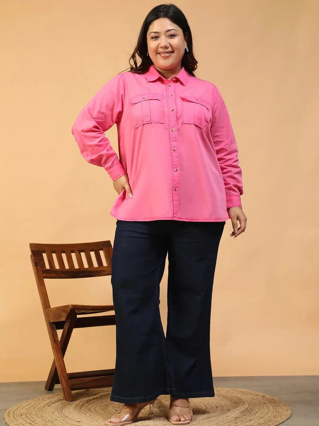 A woman wearing a bright pink button-up shirt with a collar and two pockets, standing against a white background.