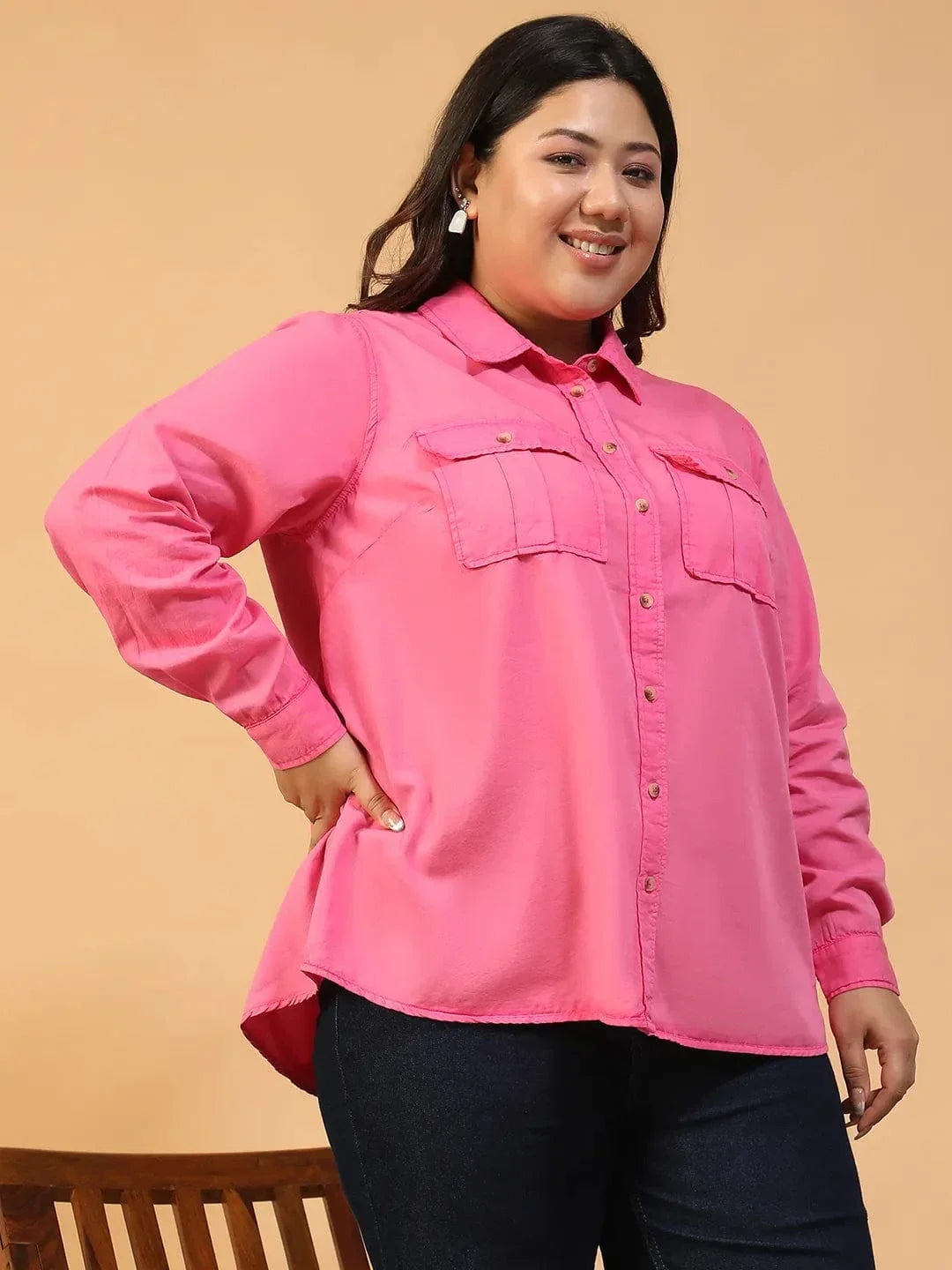 A woman wearing a bright pink button-up shirt with a collar and two pockets, standing against a white background.