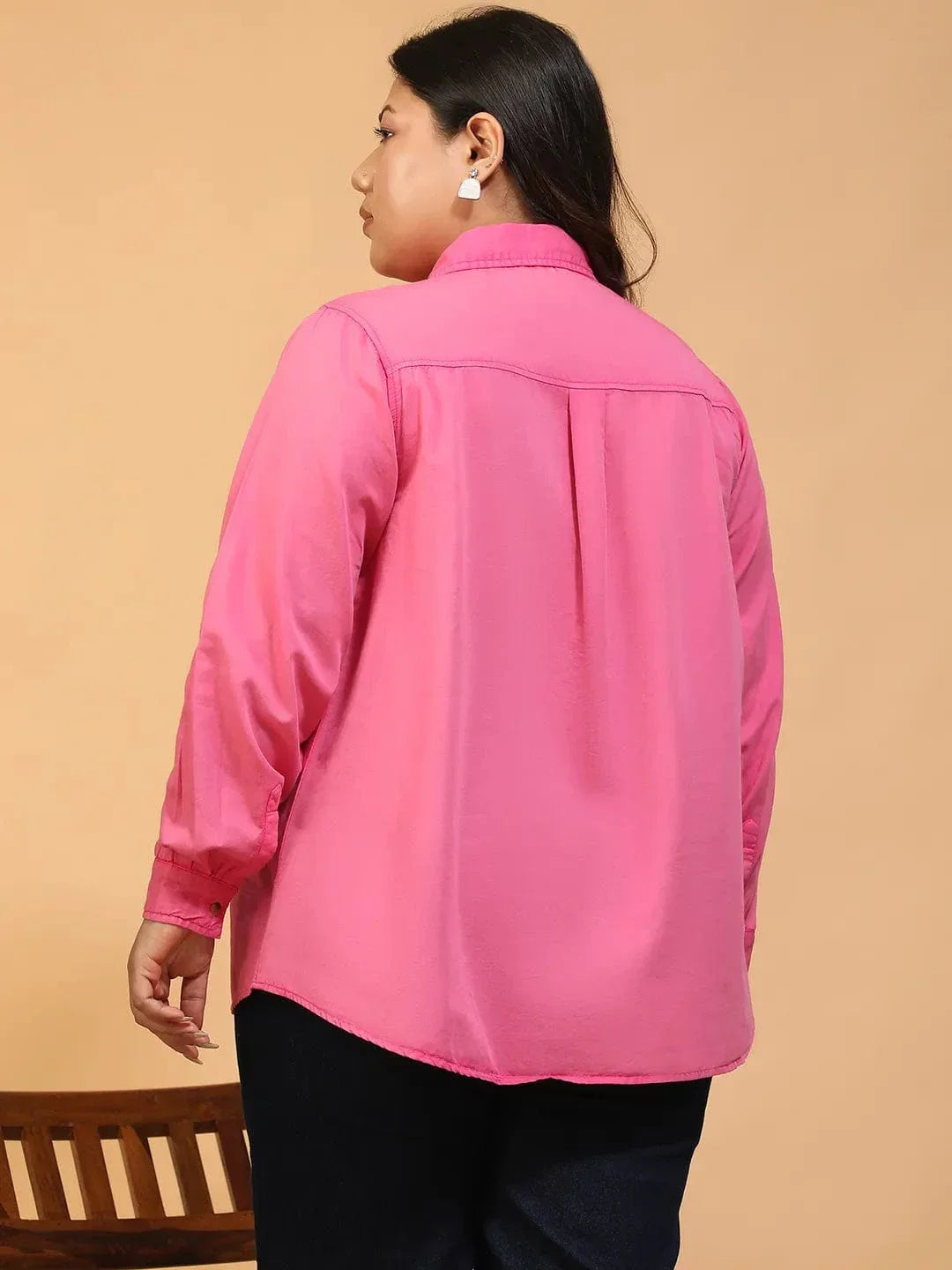 A woman wearing a bright pink button-up shirt with a collar and two pockets, standing against a white background.