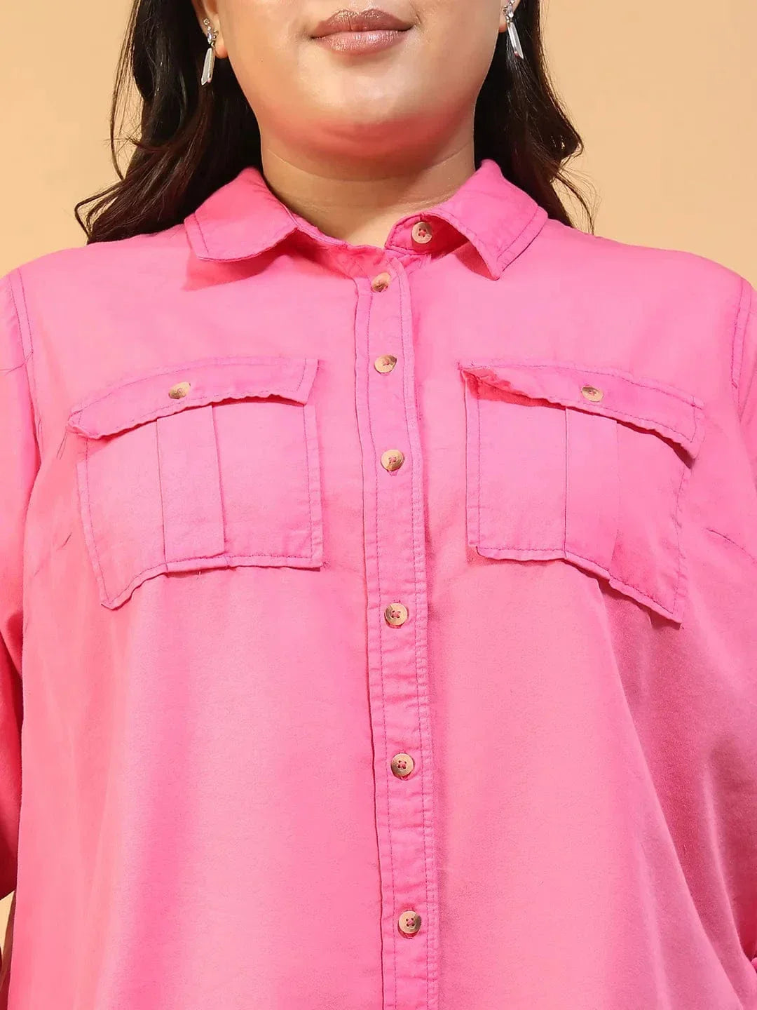 A woman wearing a bright pink button-up shirt with a collar and two pockets, standing against a white background.