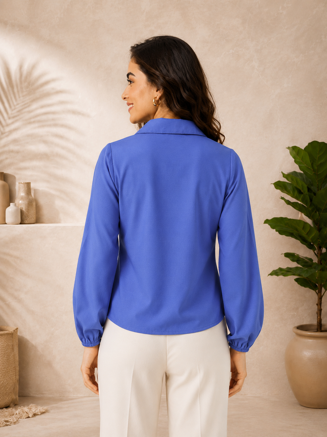 Woman wearing blue long sleeve blouse with elastic cuffs, paired with white pants, back view