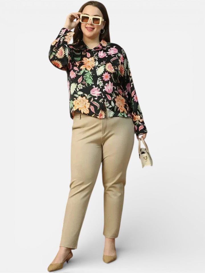 A woman wearing a black and pink floral shirt, beige pants, and large sunglasses, smiling and posing for the camera.