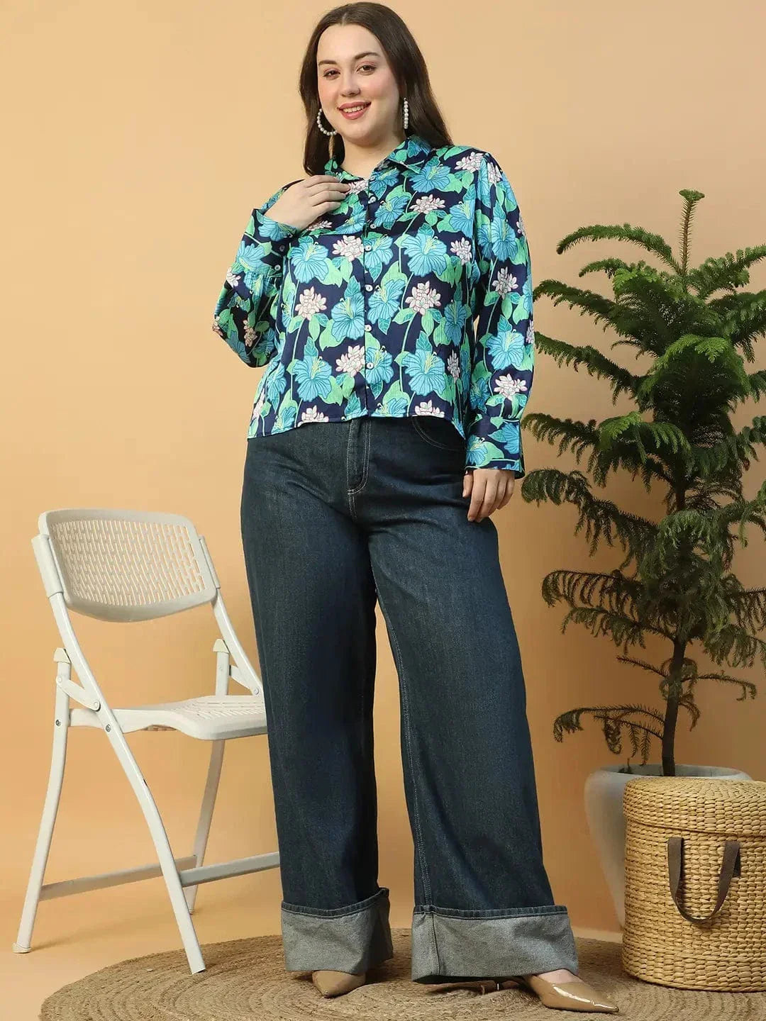 A woman wearing a floral print blouse and jeans is posing with her hand on her head.