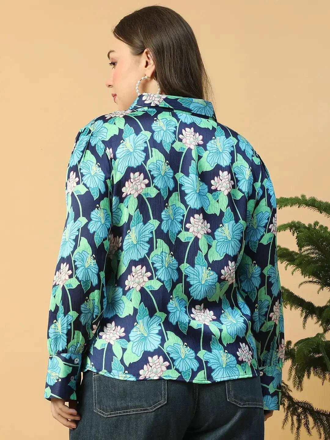 A woman wearing a floral print blouse and jeans is posing with her hand on her head.