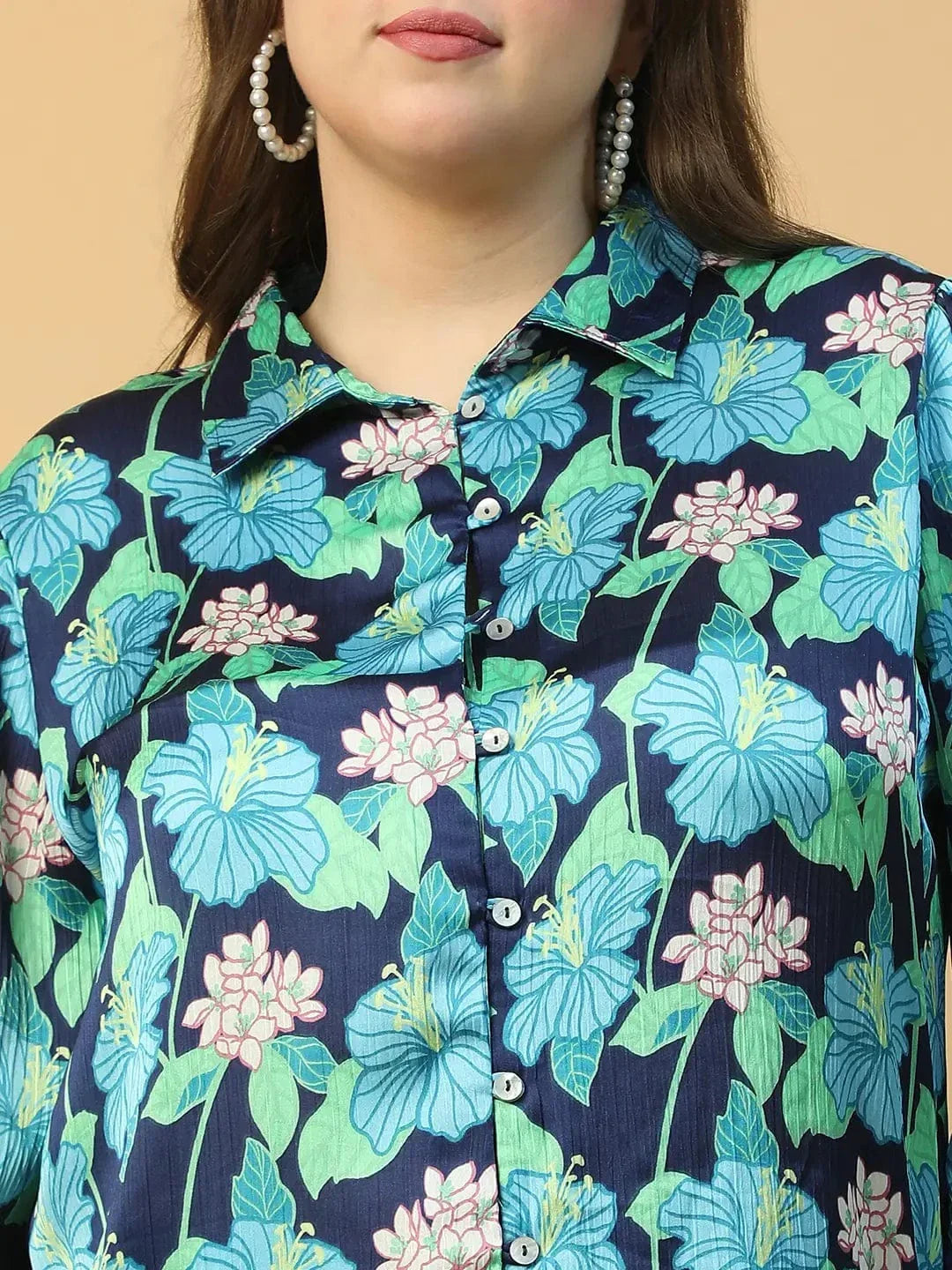 A woman wearing a floral print blouse and jeans is posing with her hand on her head.