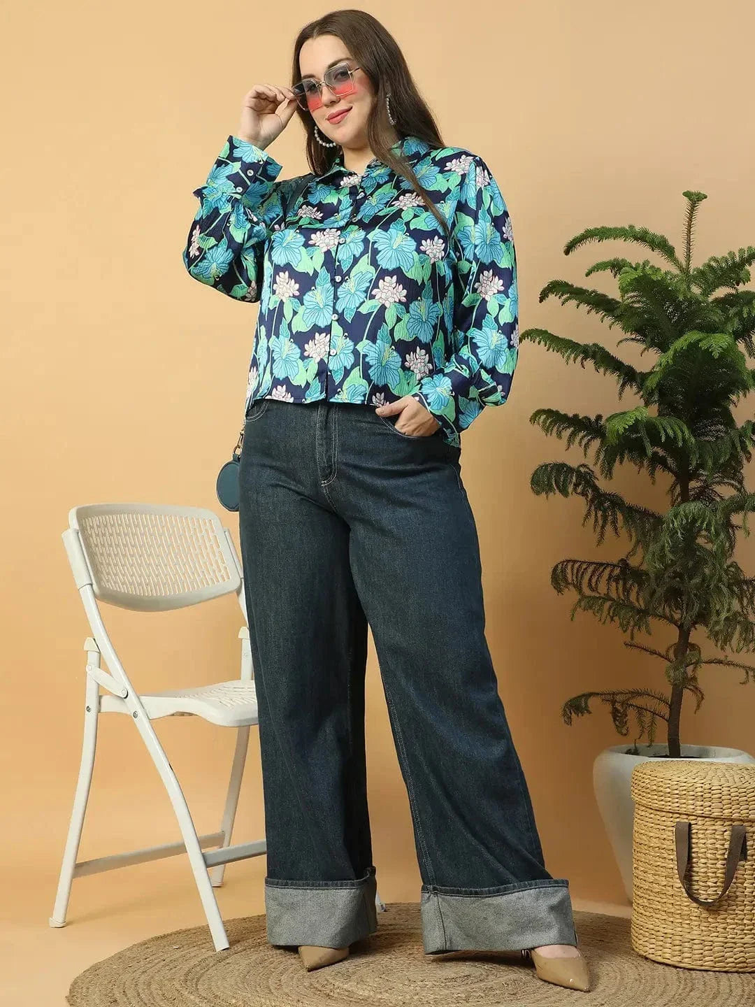 A woman wearing a floral print blouse and jeans is posing with her hand on her head.