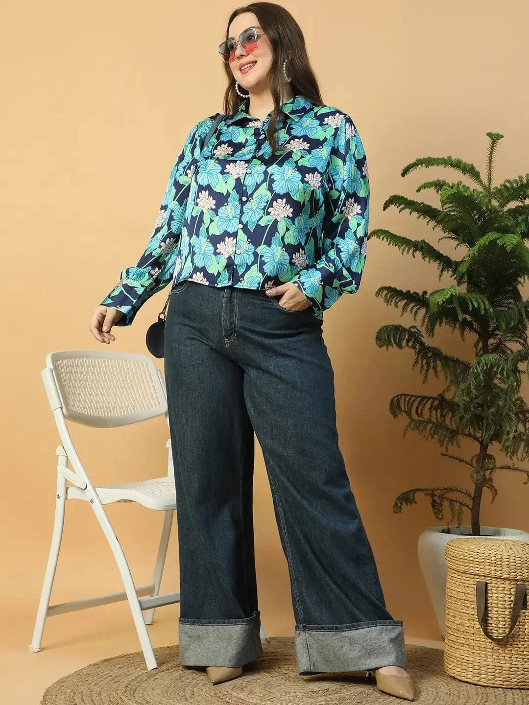 A woman wearing a floral print blouse and jeans is posing with her hand on her head.