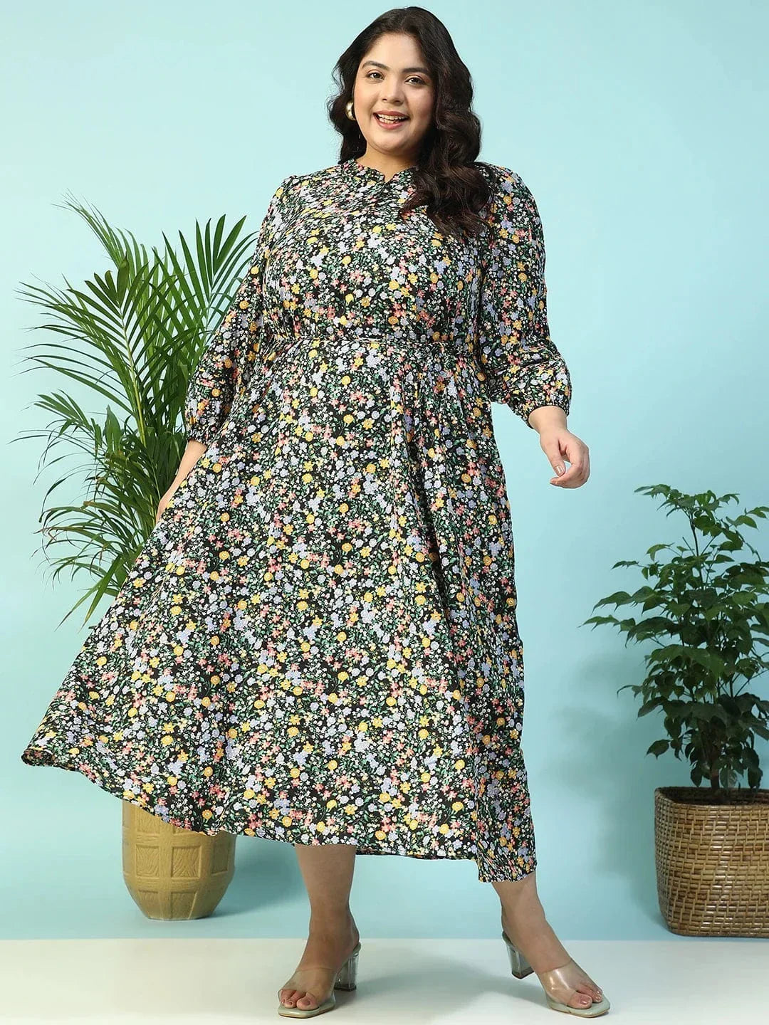 A woman wearing a long, floral print dress with puff sleeves and a tie at the neckline, smiling at the camera.