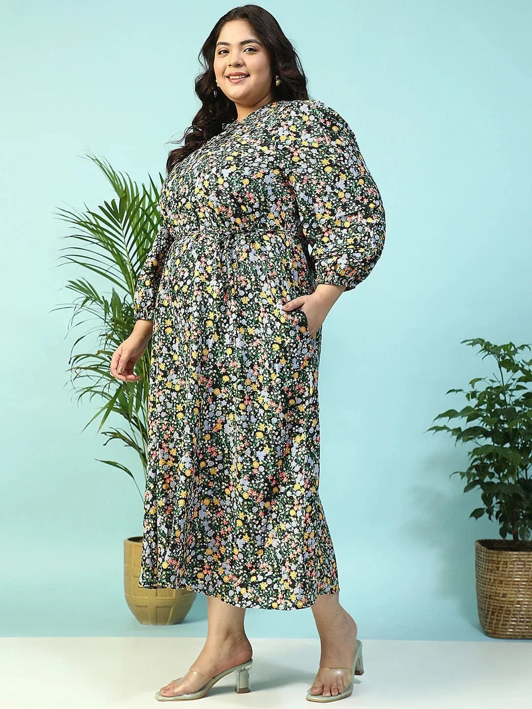 A woman wearing a long, floral print dress with puff sleeves and a tie at the neckline, smiling at the camera.