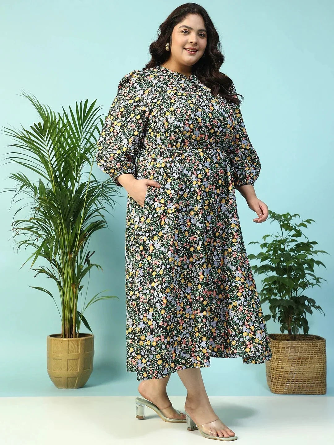 A woman wearing a long, floral print dress with puff sleeves and a tie at the neckline, smiling at the camera.