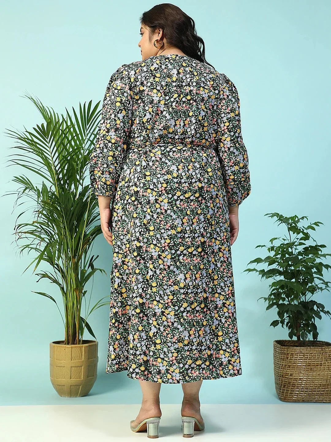 A woman wearing a long, floral print dress with puff sleeves and a tie at the neckline, smiling at the camera.