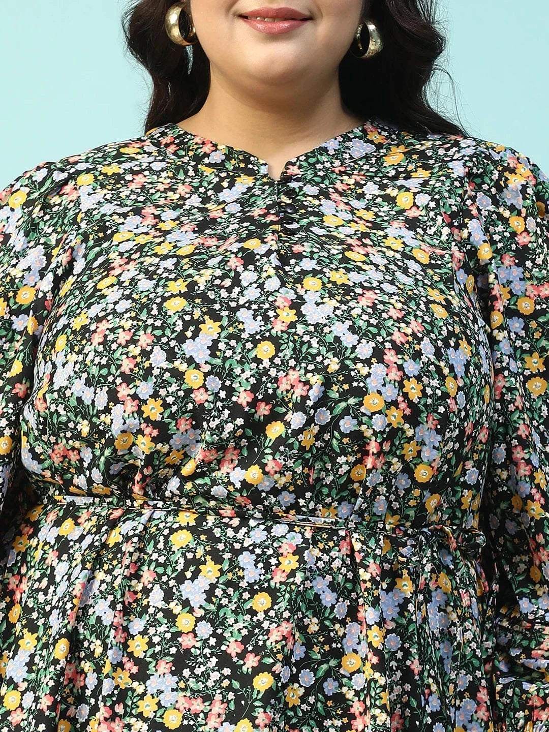 A woman wearing a long, floral print dress with puff sleeves and a tie at the neckline, smiling at the camera.