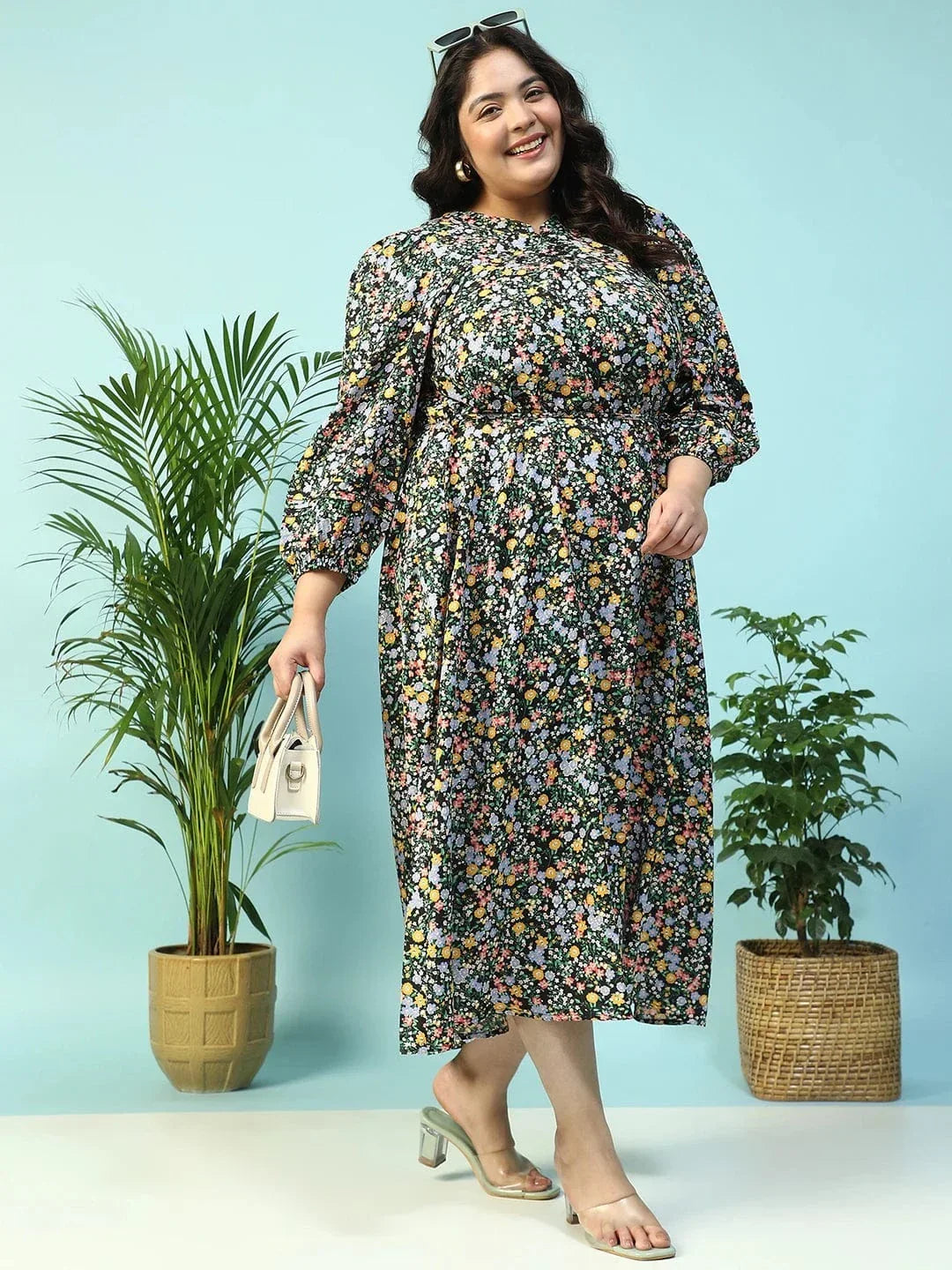 A woman wearing a long, floral print dress with puff sleeves and a tie at the neckline, smiling at the camera.