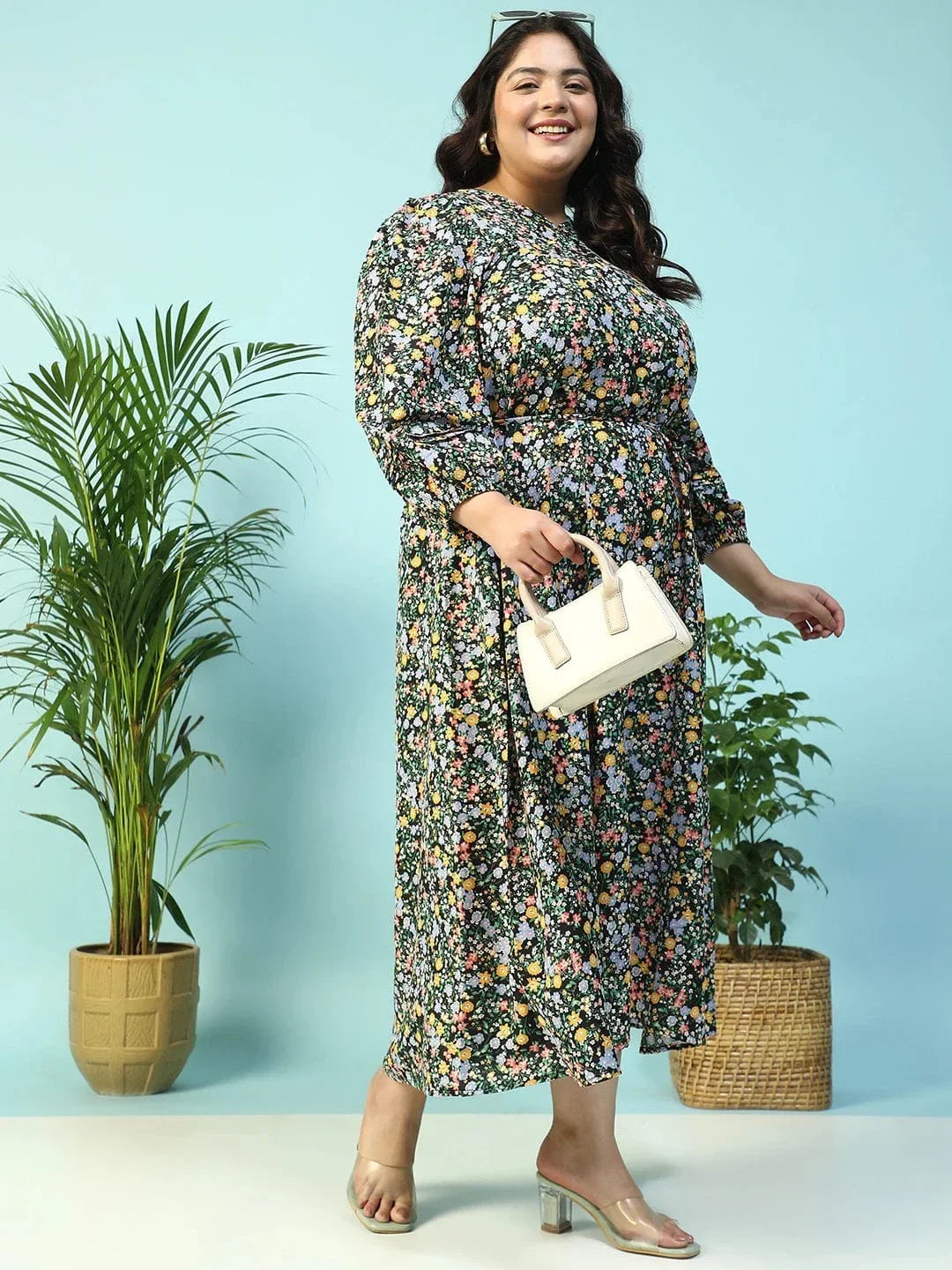 A woman wearing a long, floral print dress with puff sleeves and a tie at the neckline, smiling at the camera.