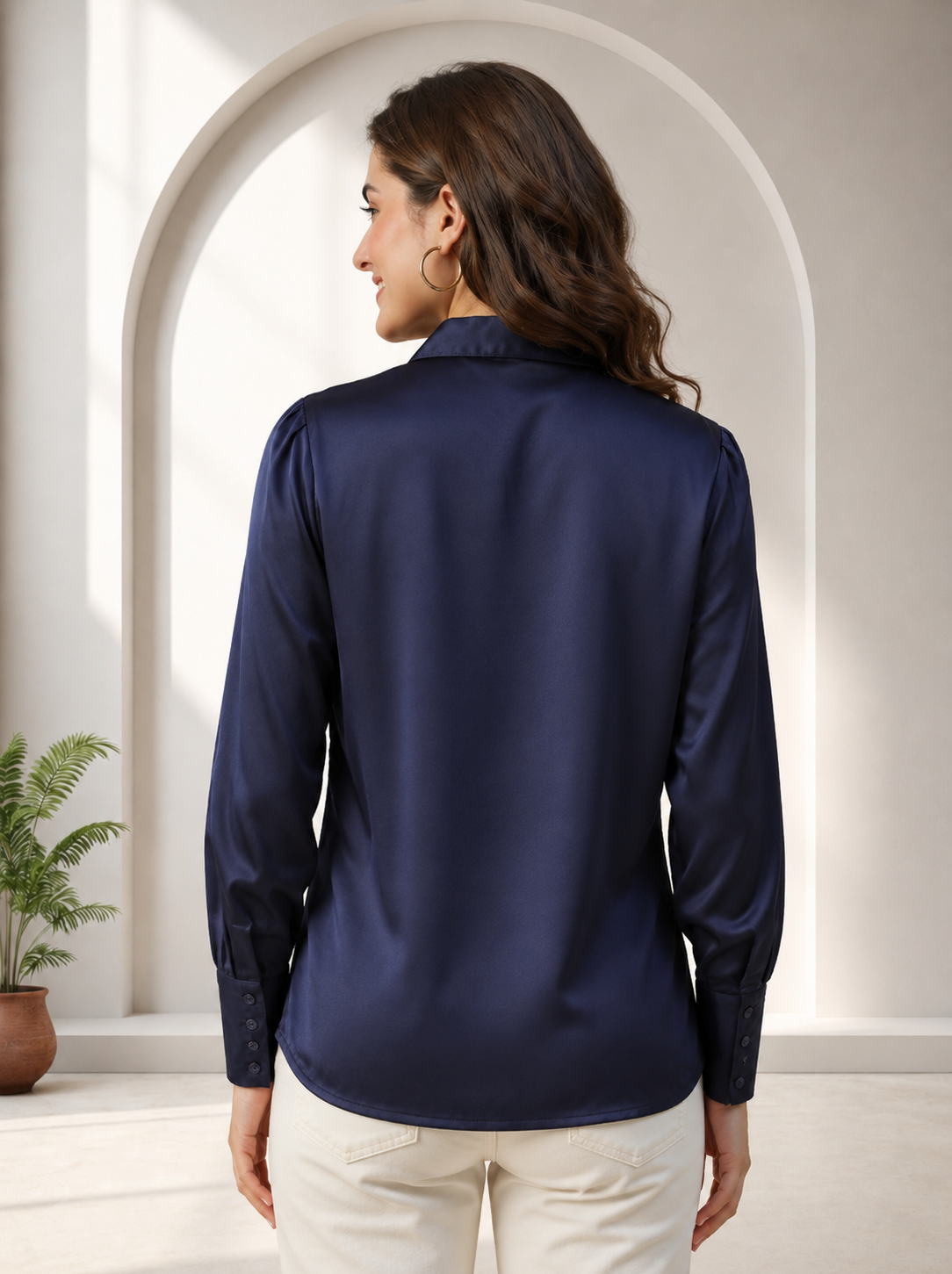 Navy blue satin long sleeve blouse for women, back view, paired with cream pants in modern setting