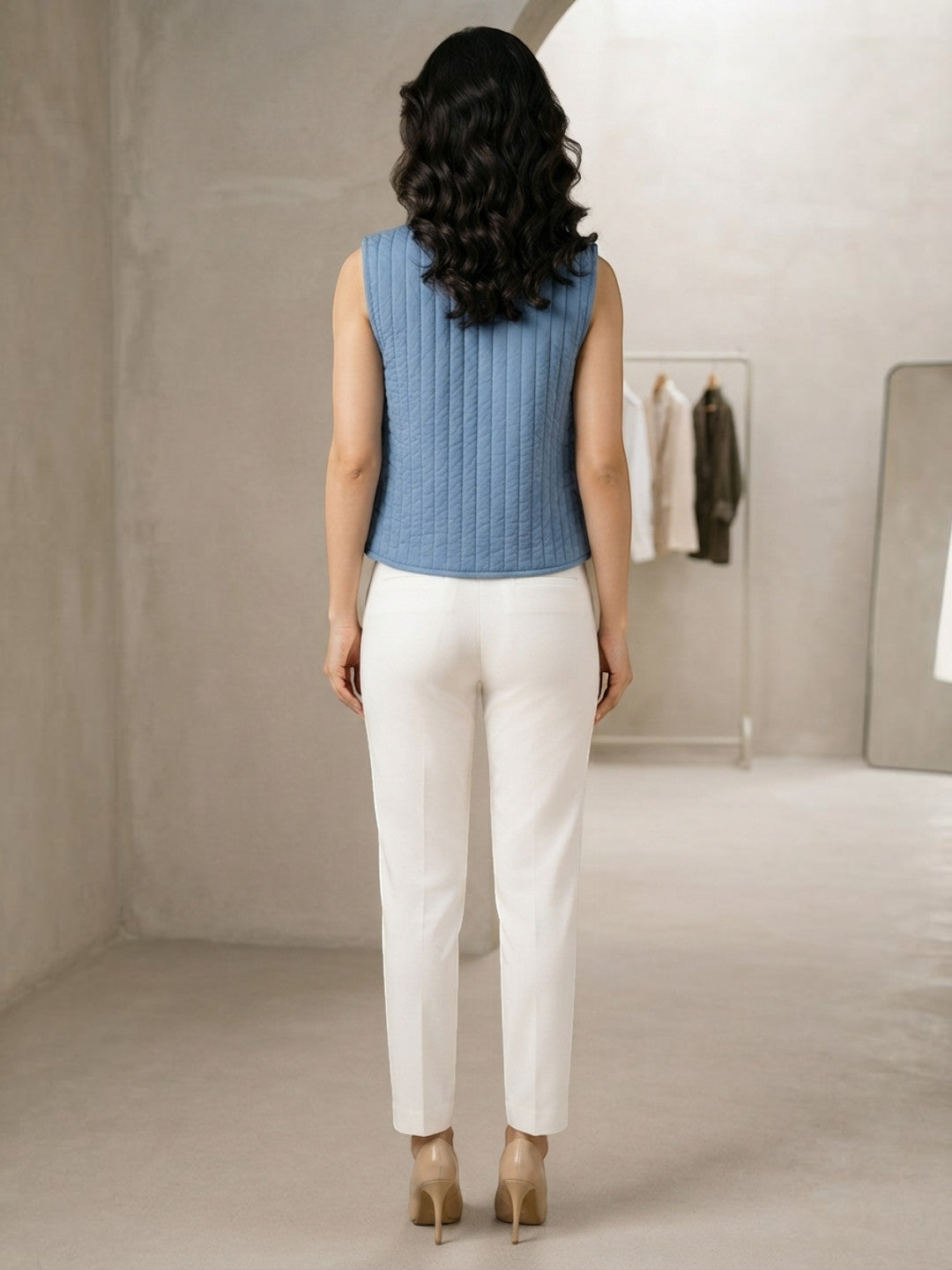 Woman wearing blue quilted sleeveless top and white tailored pants, back view, modern office style