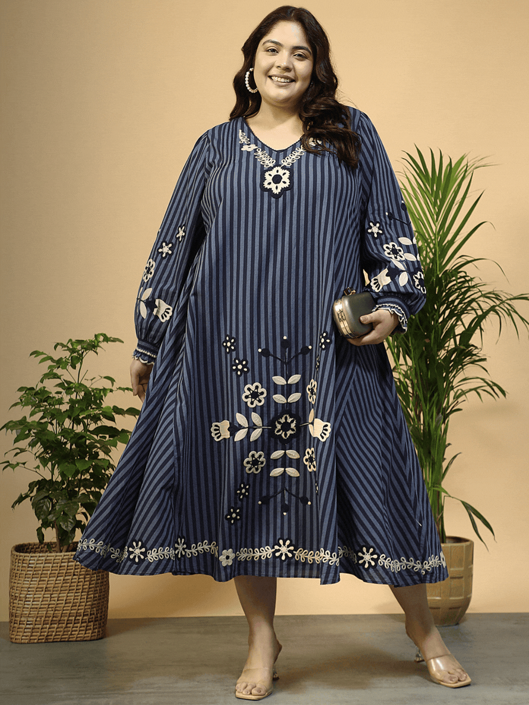 A woman wearing a long, striped dress with floral embroidery and puffed sleeves, smiling at the camera.