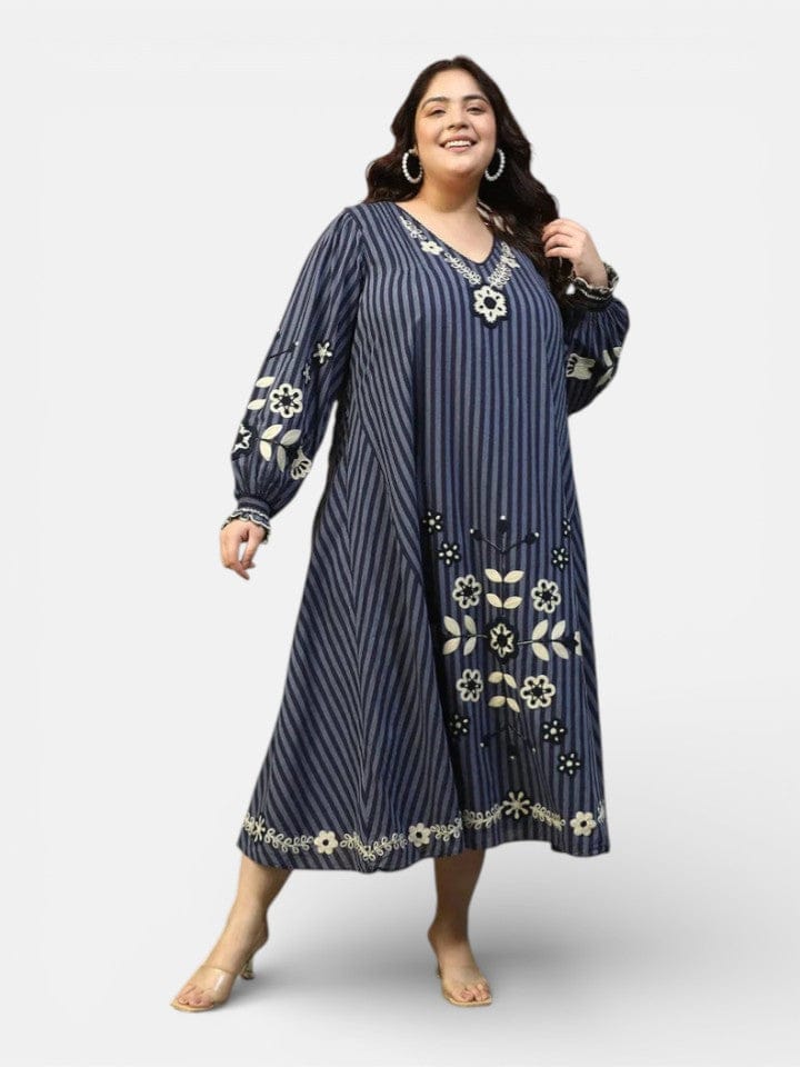 A woman wearing a long, striped dress with floral embroidery and puffed sleeves, smiling at the camera.