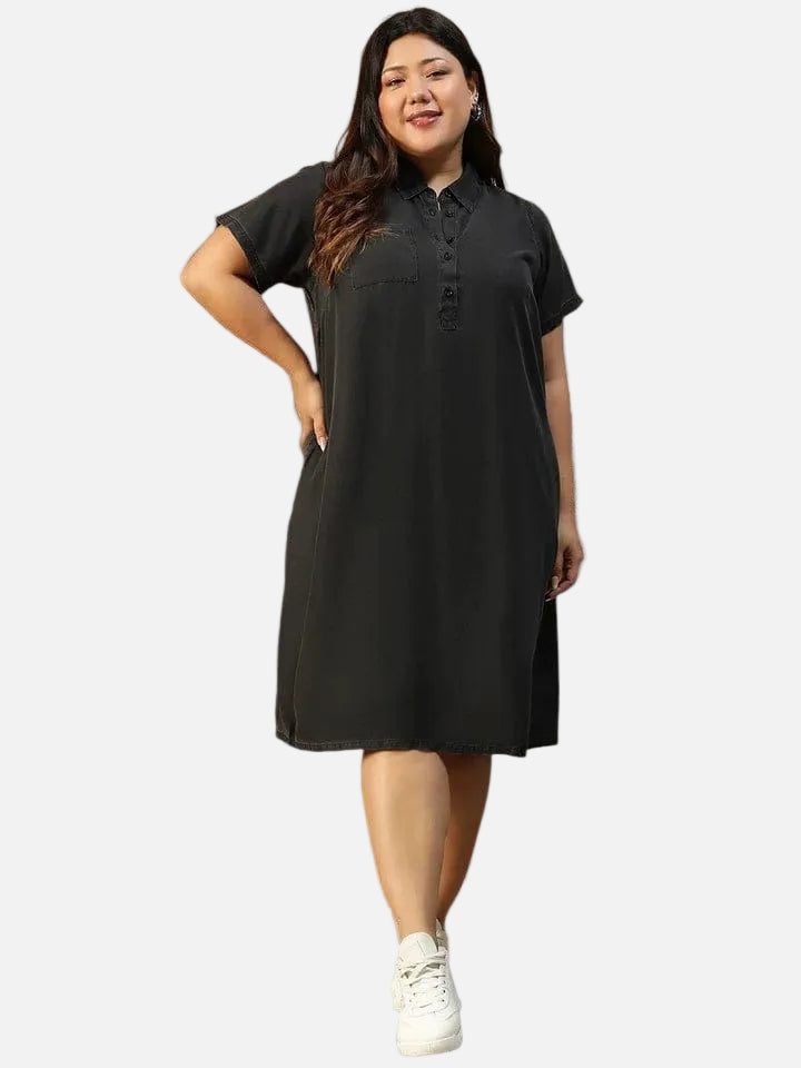 A woman wearing a black dress with short sleeves and a collar, posing with her hand on her hip and smiling.