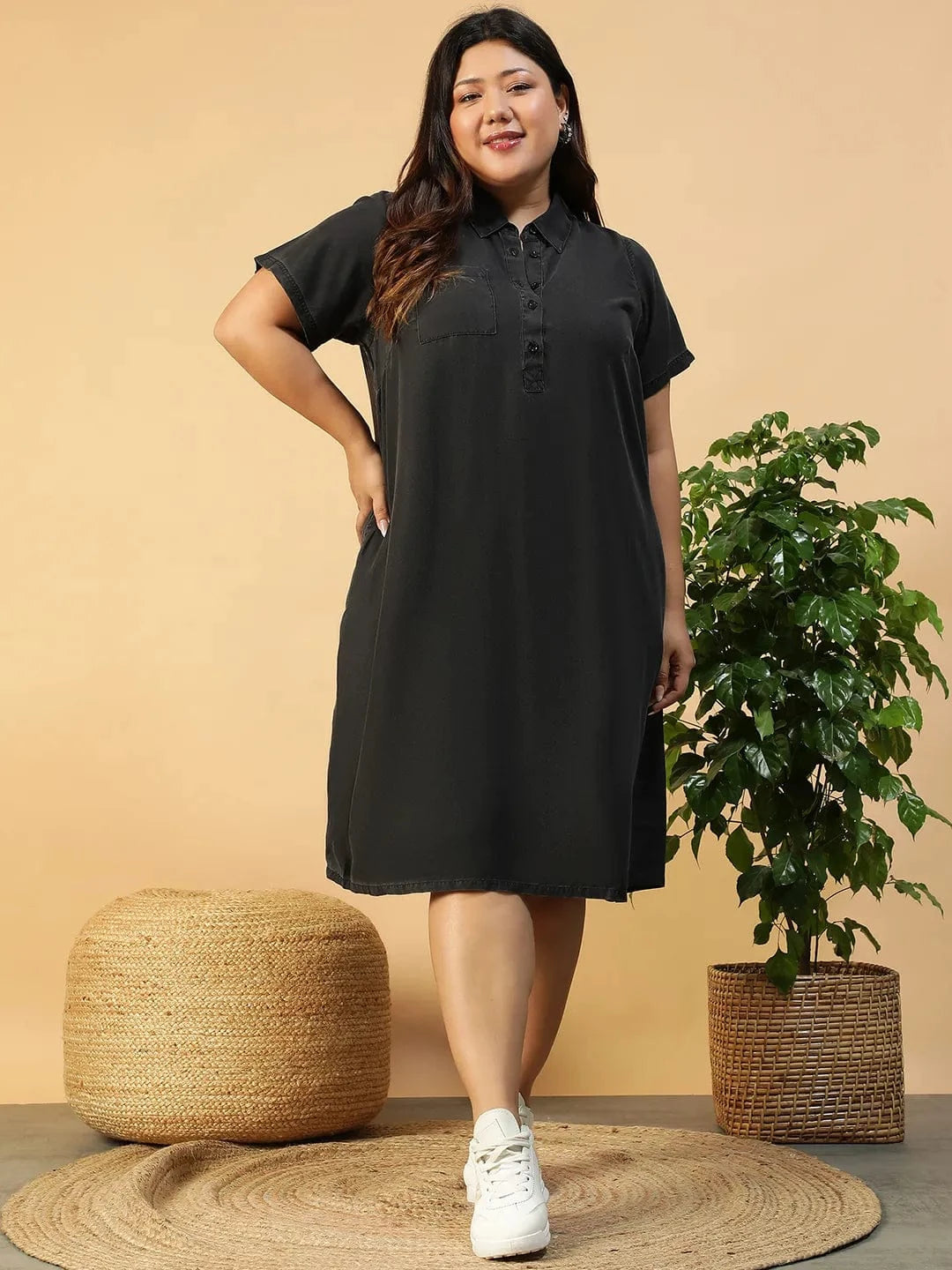 A woman wearing a black dress with short sleeves and a collar, posing with her hand on her hip and smiling.