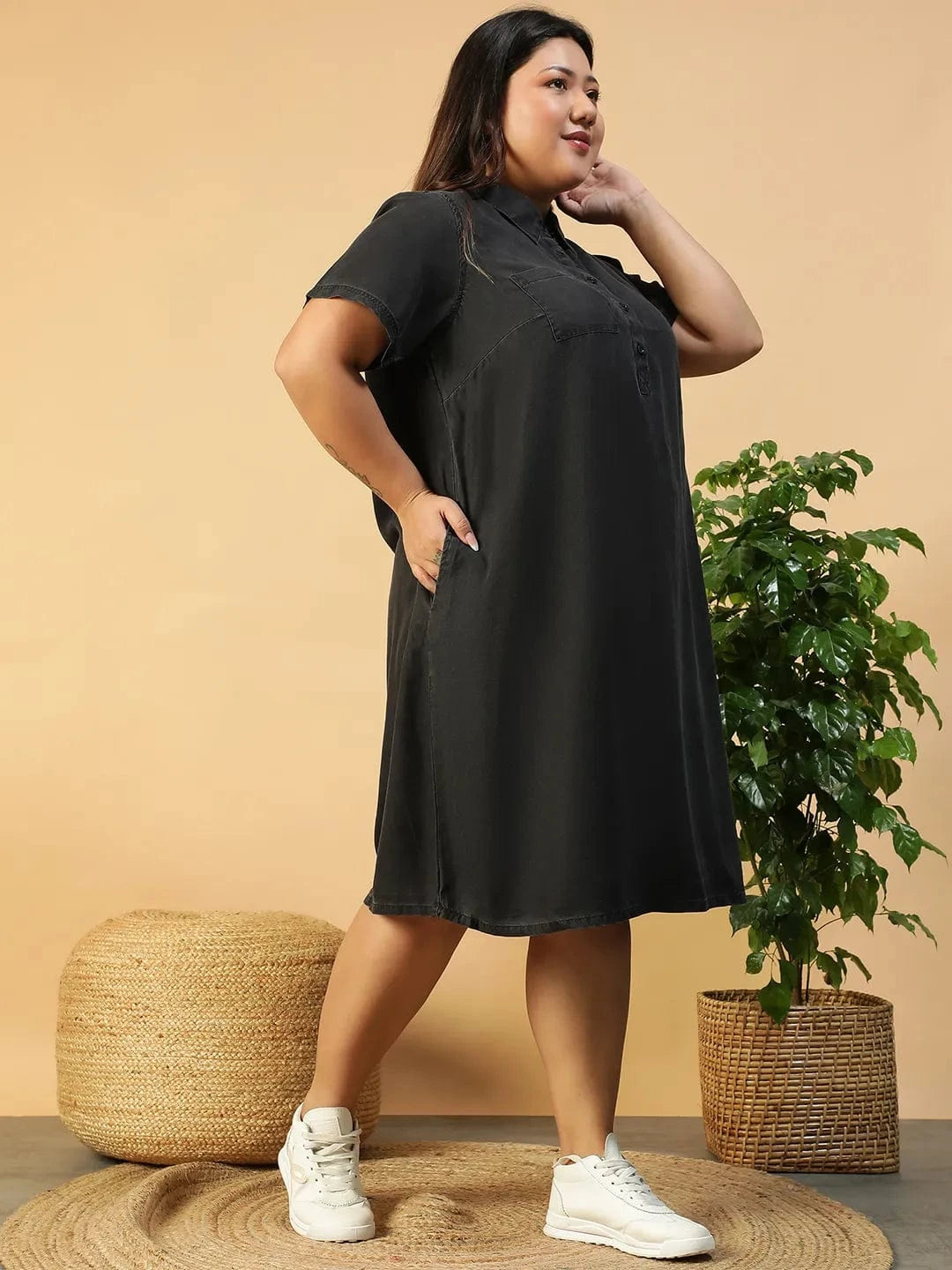 A woman wearing a black dress with short sleeves and a collar, posing with her hand on her hip and smiling.