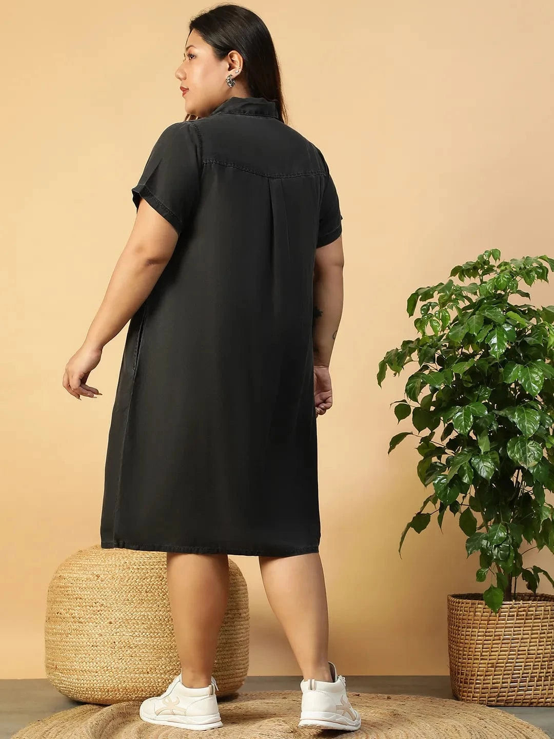 A woman wearing a black dress with short sleeves and a collar, posing with her hand on her hip and smiling.