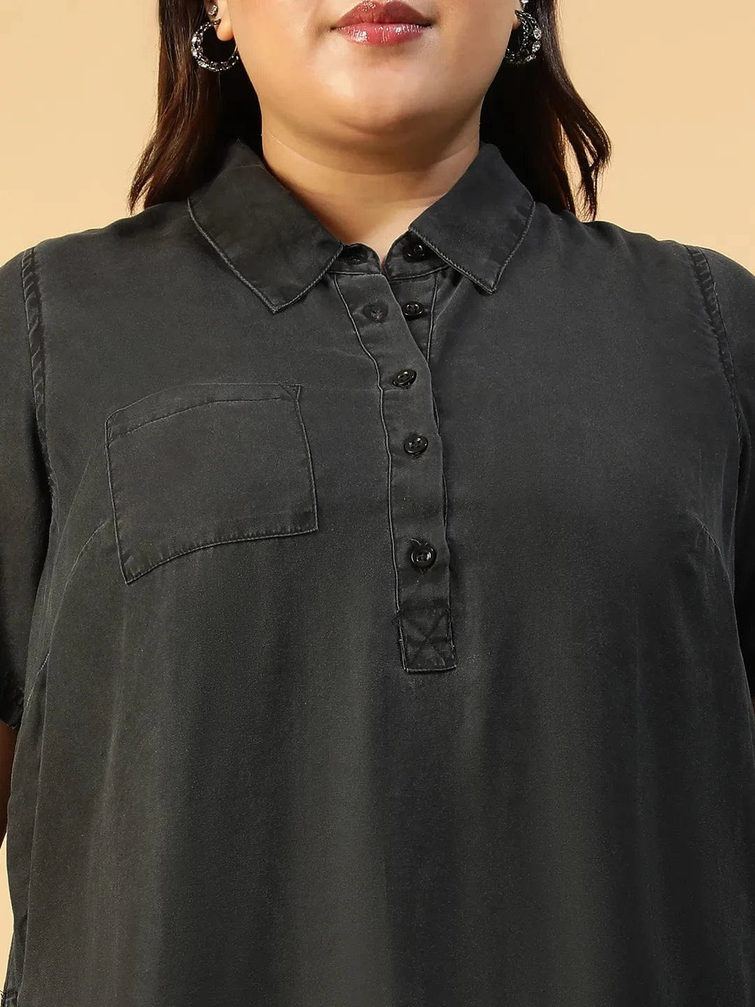 A woman wearing a black dress with short sleeves and a collar, posing with her hand on her hip and smiling.