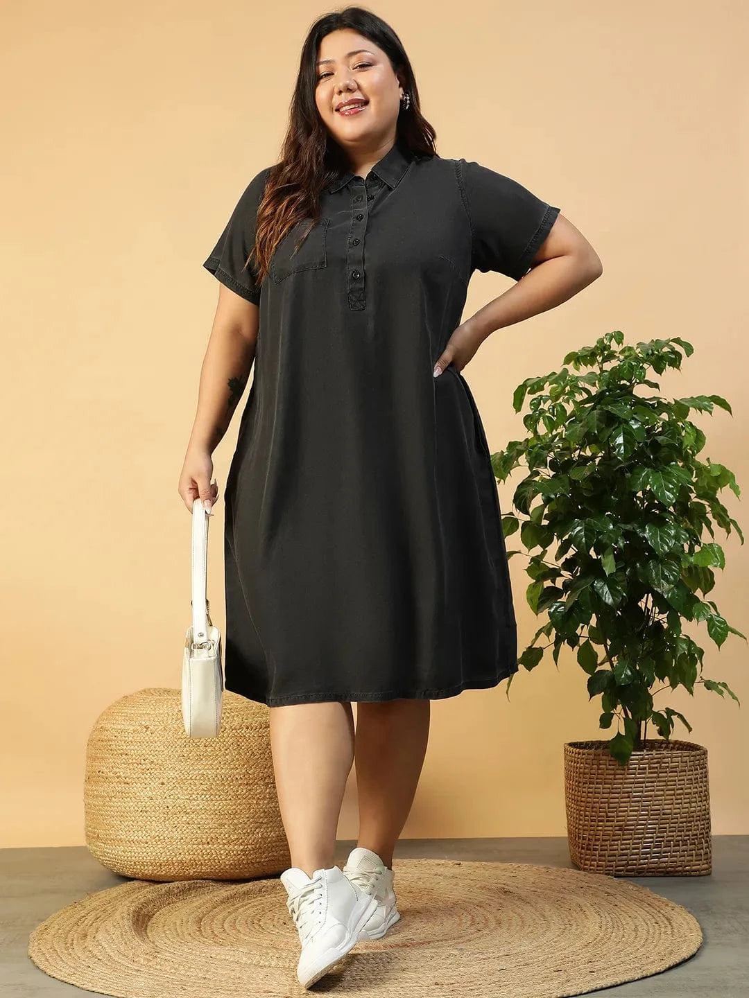 A woman wearing a black dress with short sleeves and a collar, posing with her hand on her hip and smiling.