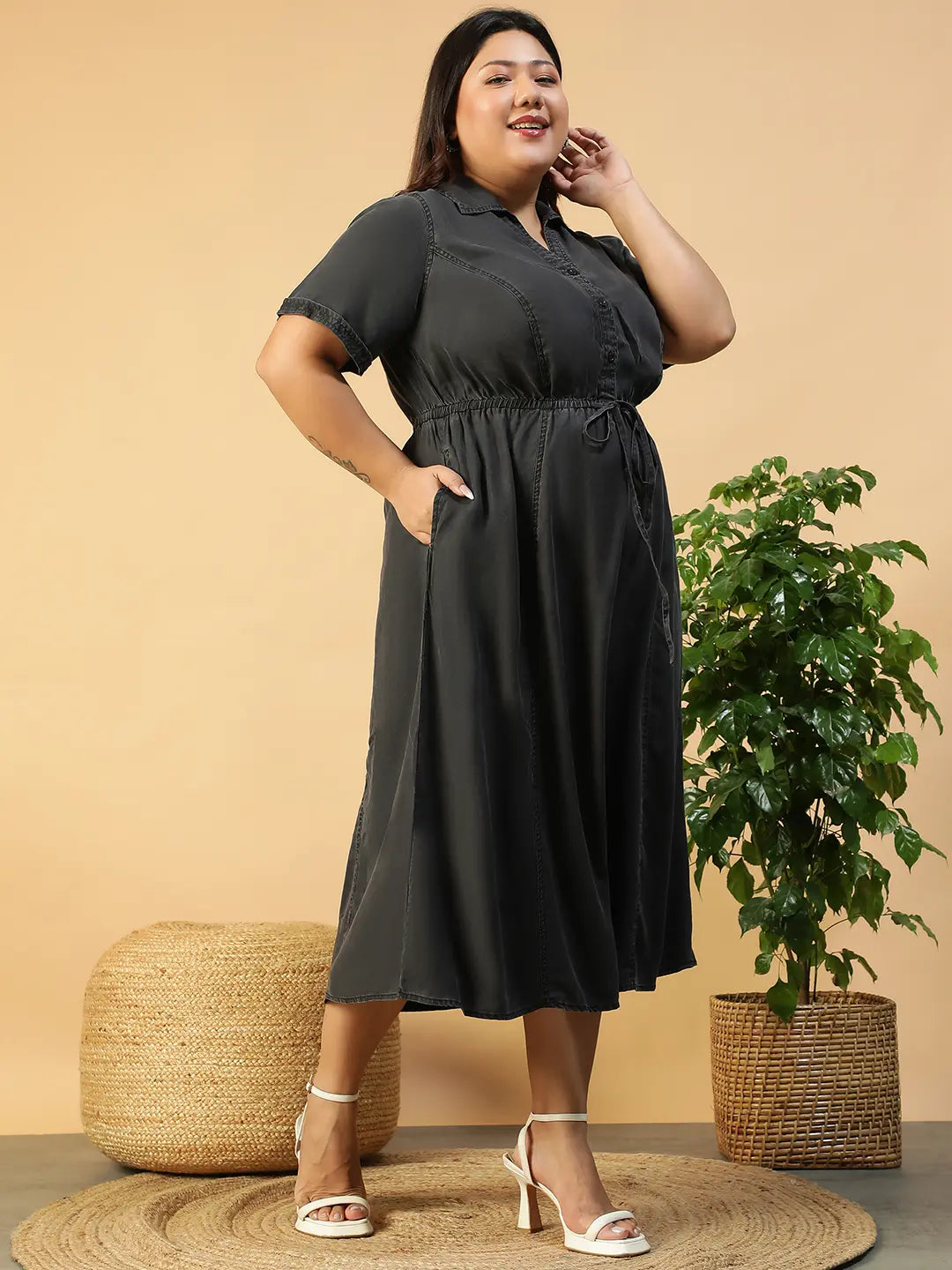 A woman wearing a gray dress with a tie waist and short sleeves, posing with her hand on her head.