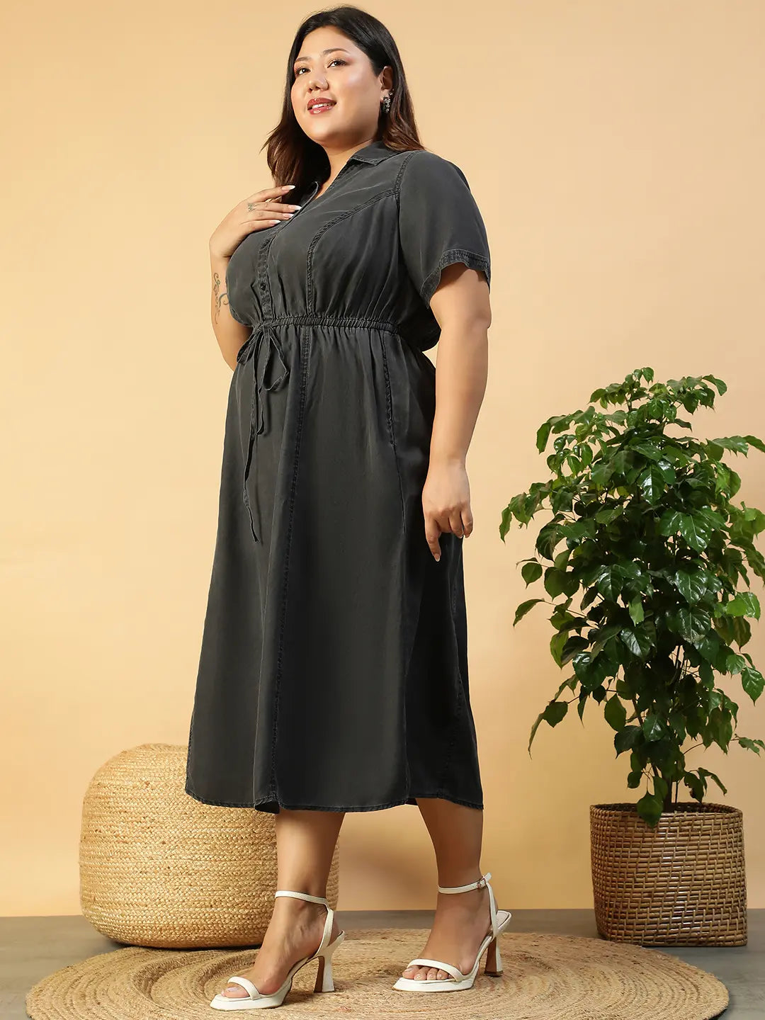 A woman wearing a gray dress with a tie waist and short sleeves, posing with her hand on her head.