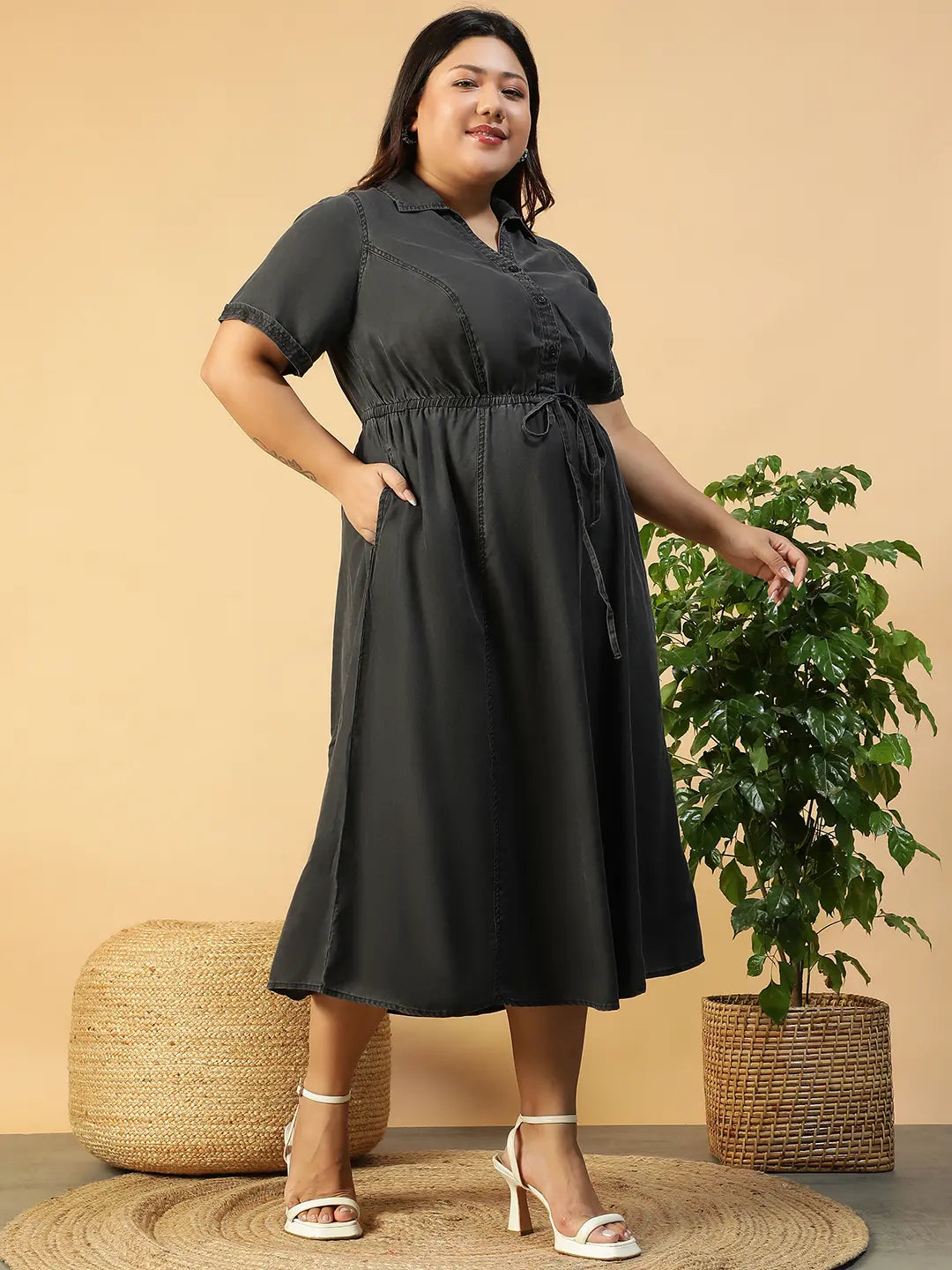 A woman wearing a gray dress with a tie waist and short sleeves, posing with her hand on her head.