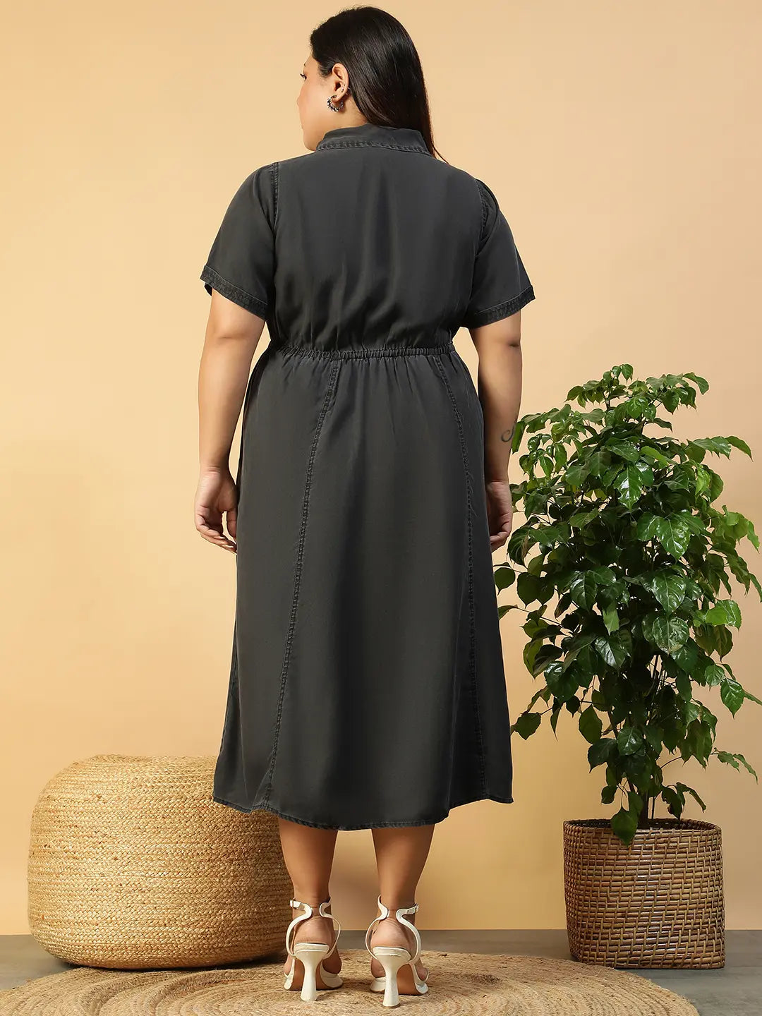A woman wearing a gray dress with a tie waist and short sleeves, posing with her hand on her head.