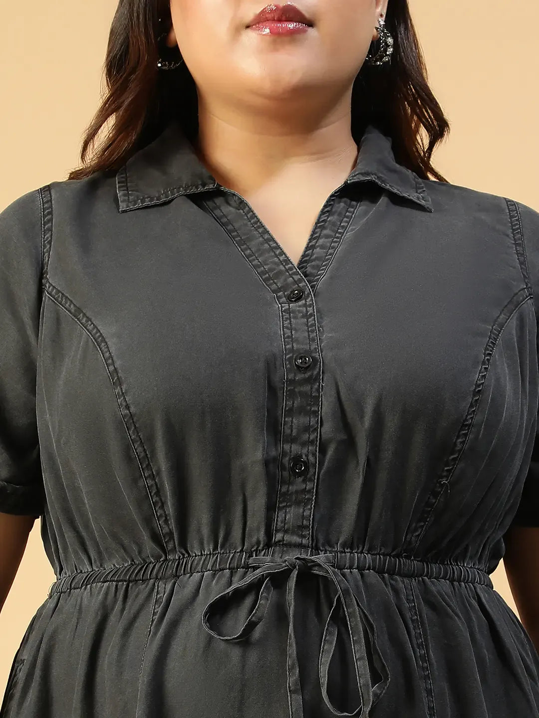 A woman wearing a gray dress with a tie waist and short sleeves, posing with her hand on her head.