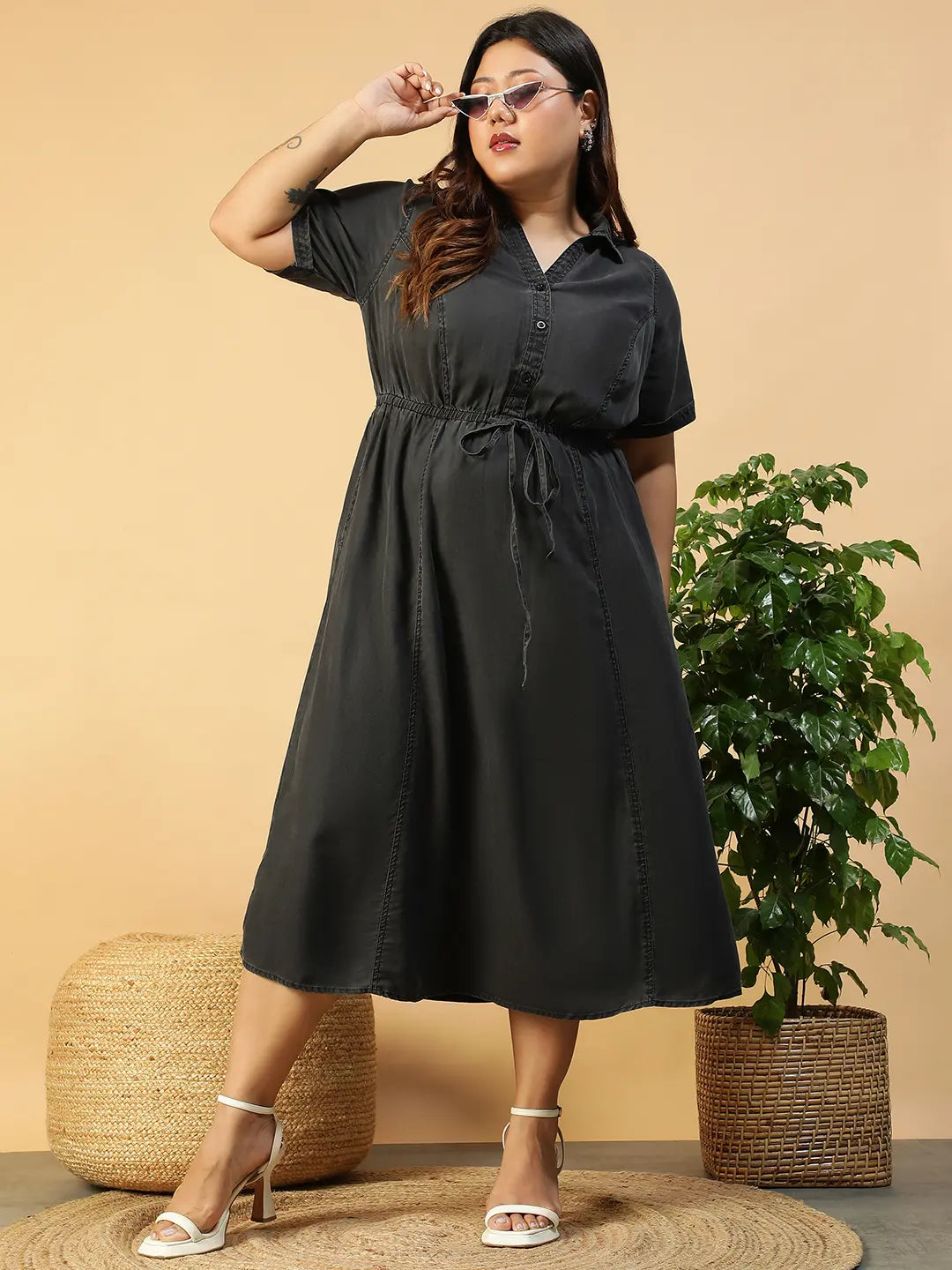 A woman wearing a gray dress with a tie waist and short sleeves, posing with her hand on her head.