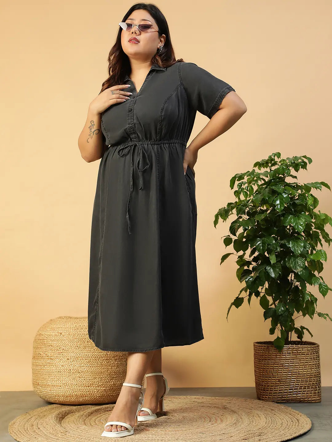 A woman wearing a gray dress with a tie waist and short sleeves, posing with her hand on her head.