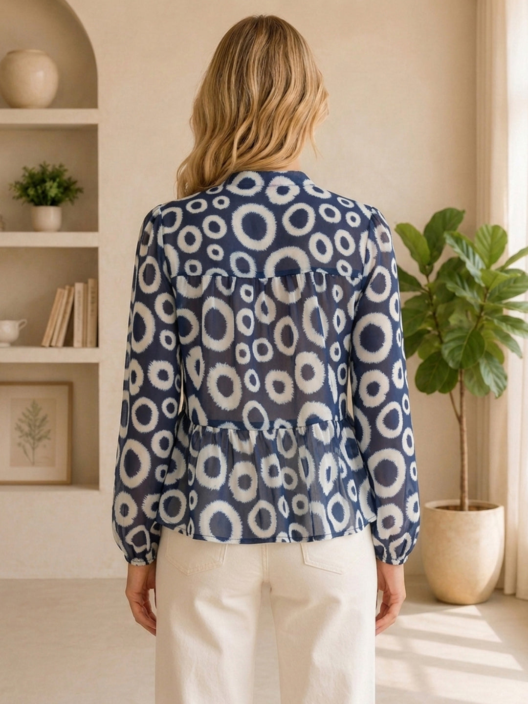 Blue and white circle print blouse with peplum hem, paired with cream pants, back view
