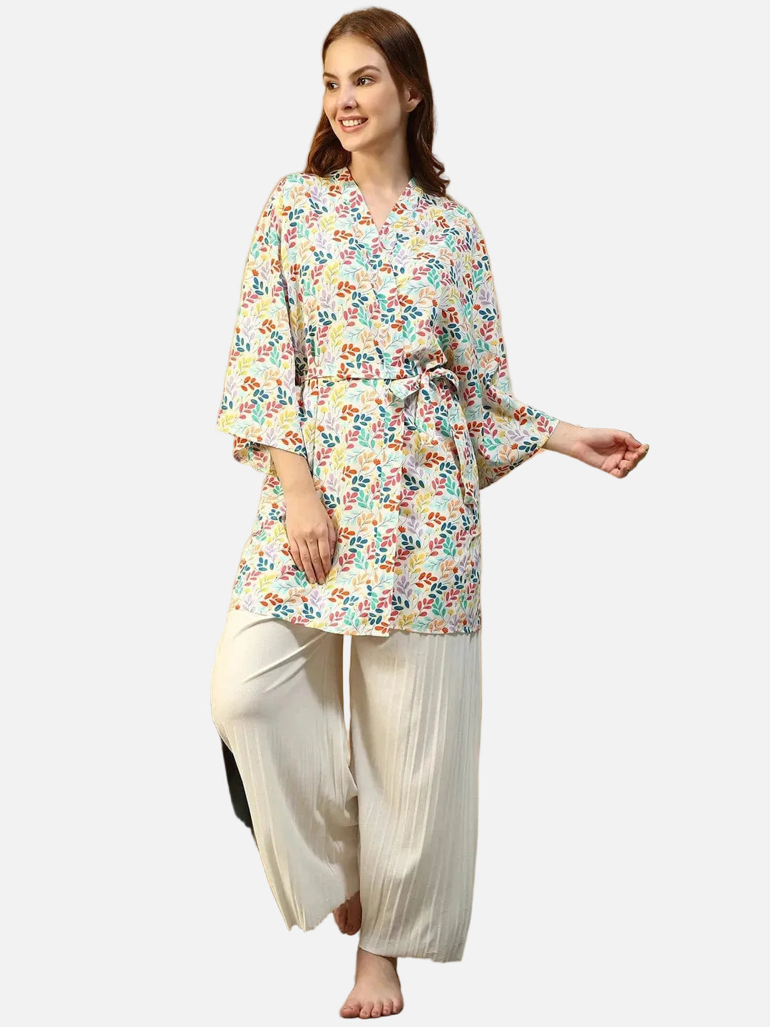 A woman wearing a colorful floral print kimono and beige pants is smiling and looking to the side.