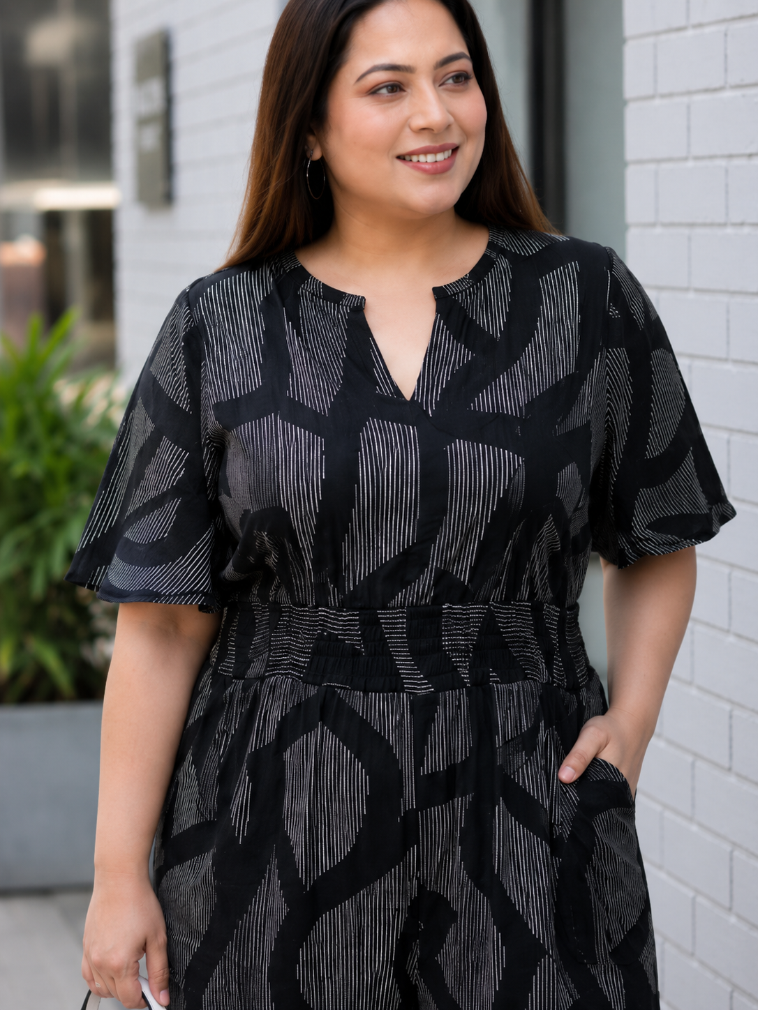 A woman wearing a black and white patterned jumpsuit is smiling and looking to the side.