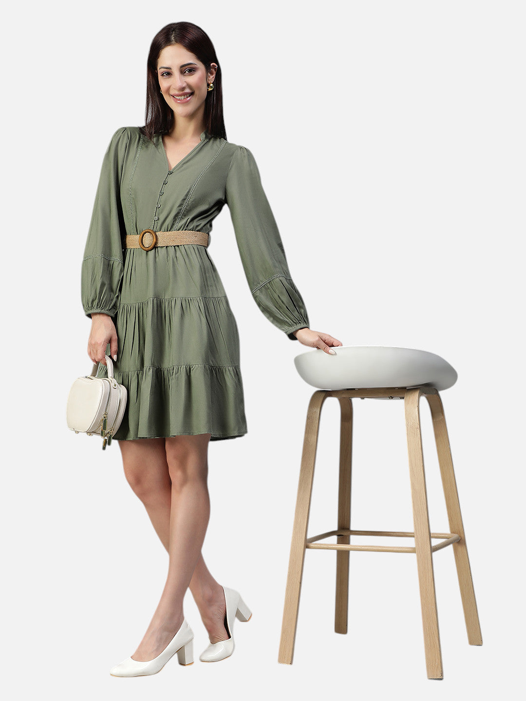 Woman in olive green belted mini dress with long sleeves, posing with a white handbag and heels