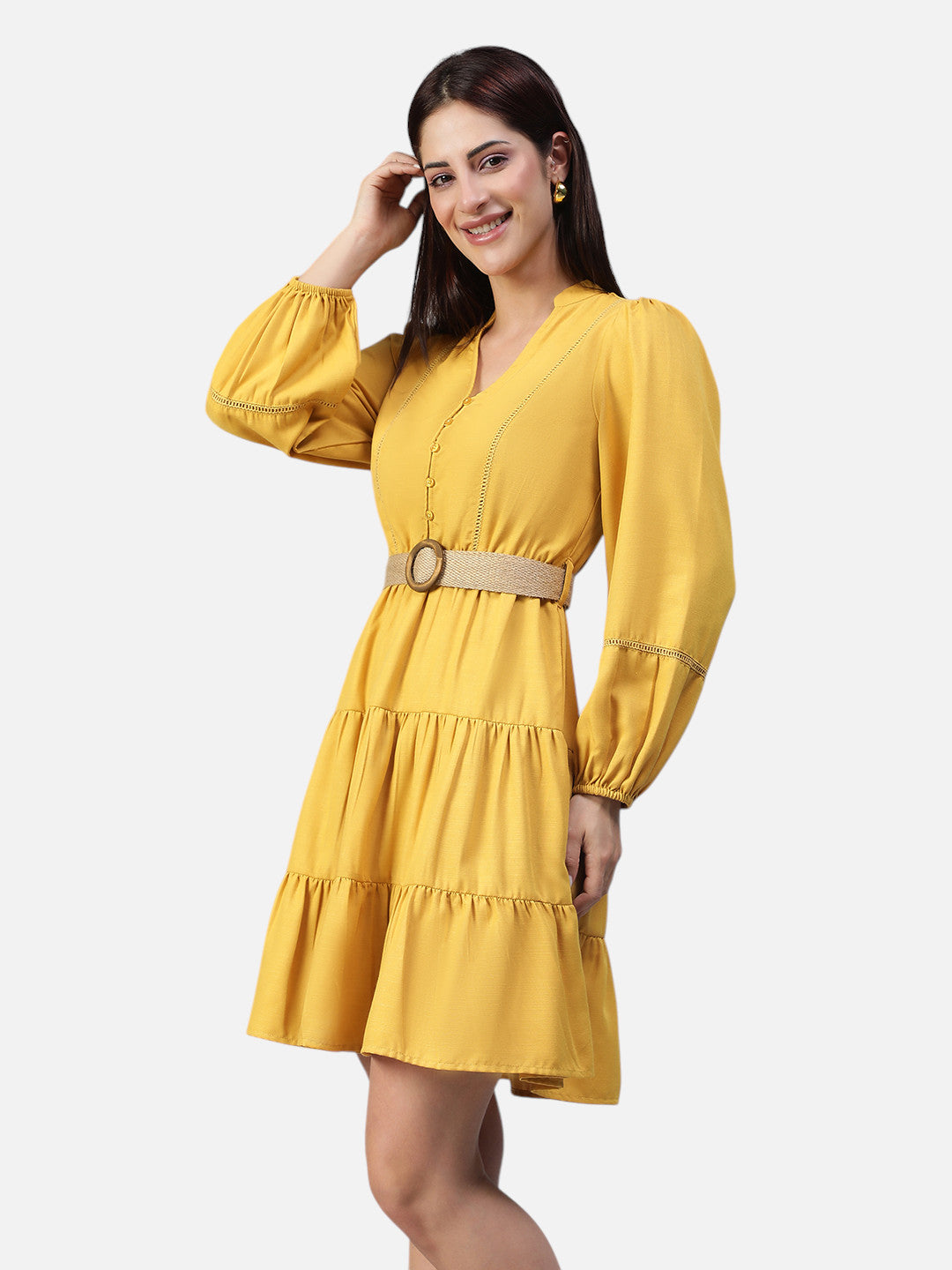 Woman wearing a yellow belted tiered mini dress with long puff sleeves, posing against white background.