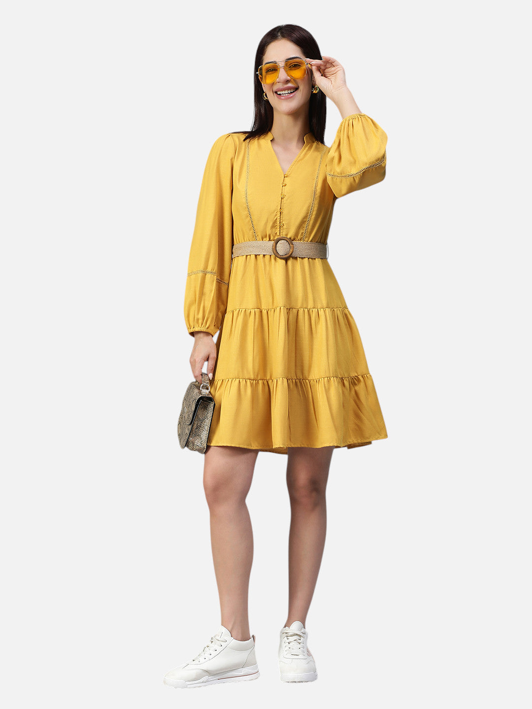 Woman in yellow belted tiered mini dress, white sneakers, and yellow sunglasses holding a handbag