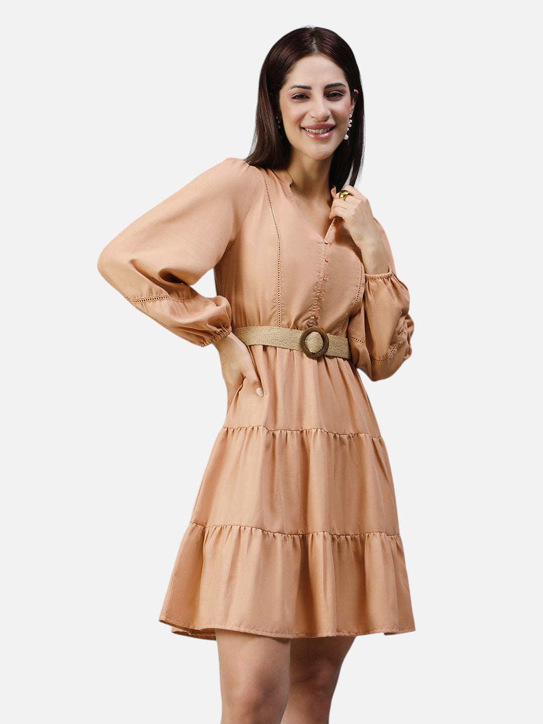 Woman wearing peach tiered mini dress with long sleeves and belted waist, standing and smiling
