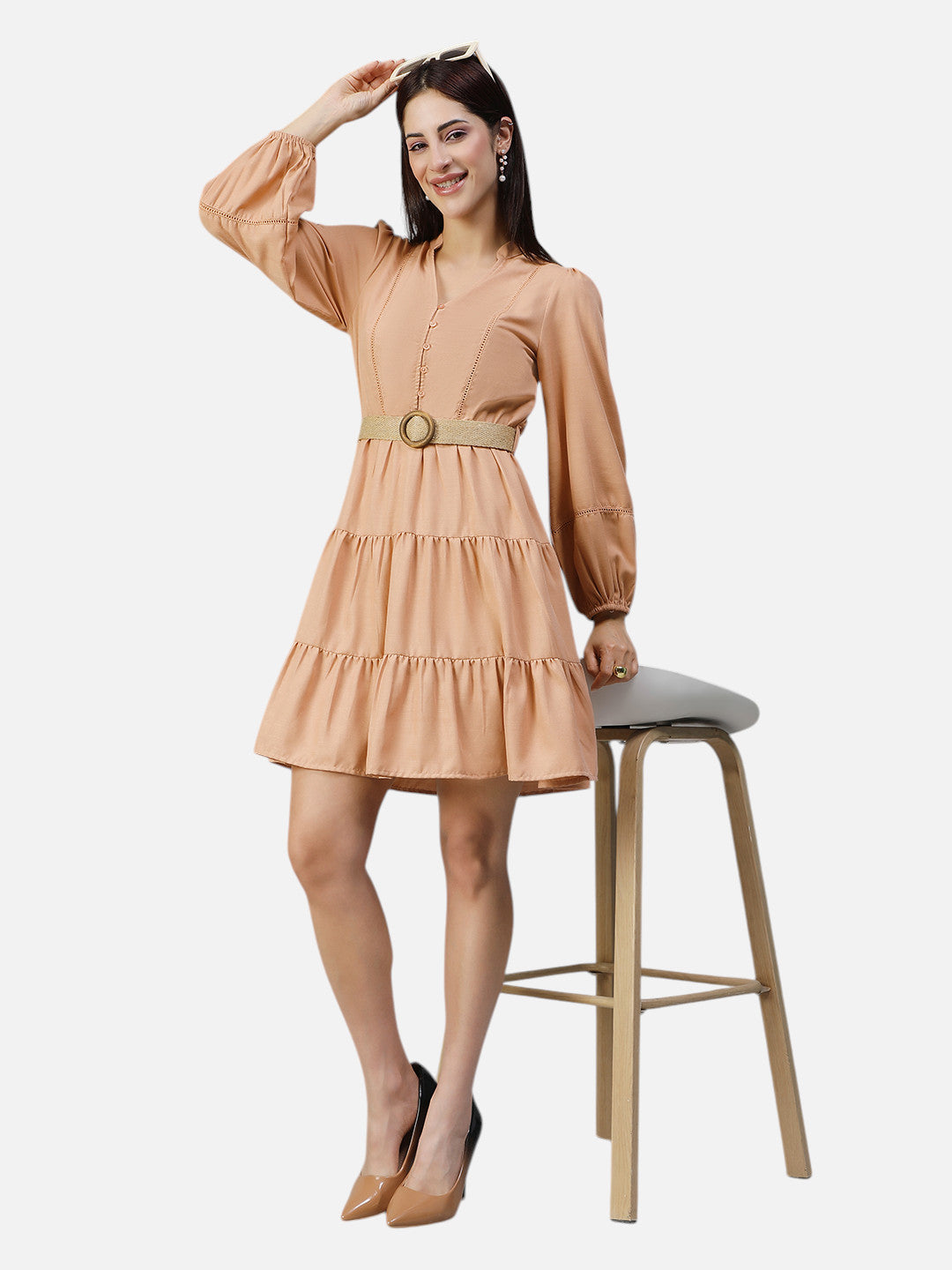Woman wearing peach long sleeve belted tiered mini dress, posing beside a wooden stool