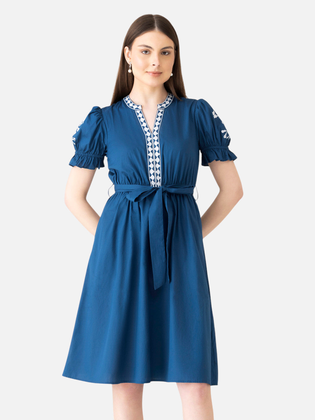 Woman wearing knee-length blue dress with puff sleeves, tie waist, and white embroidered trim