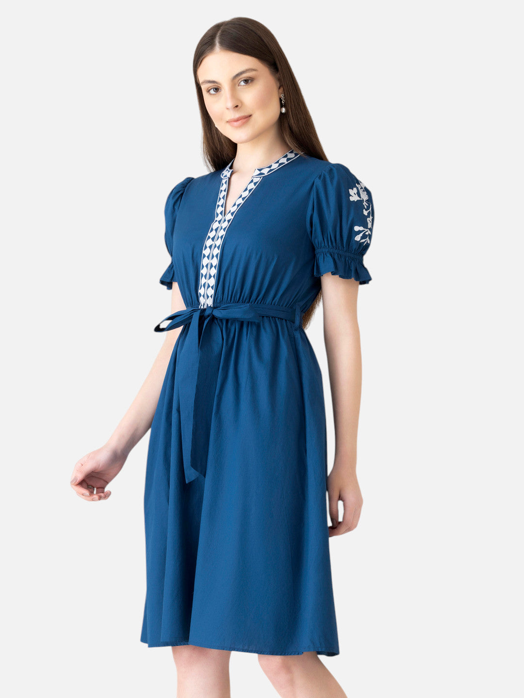 Woman wearing knee-length blue dress with puff sleeves, embroidered detail, and waist tie